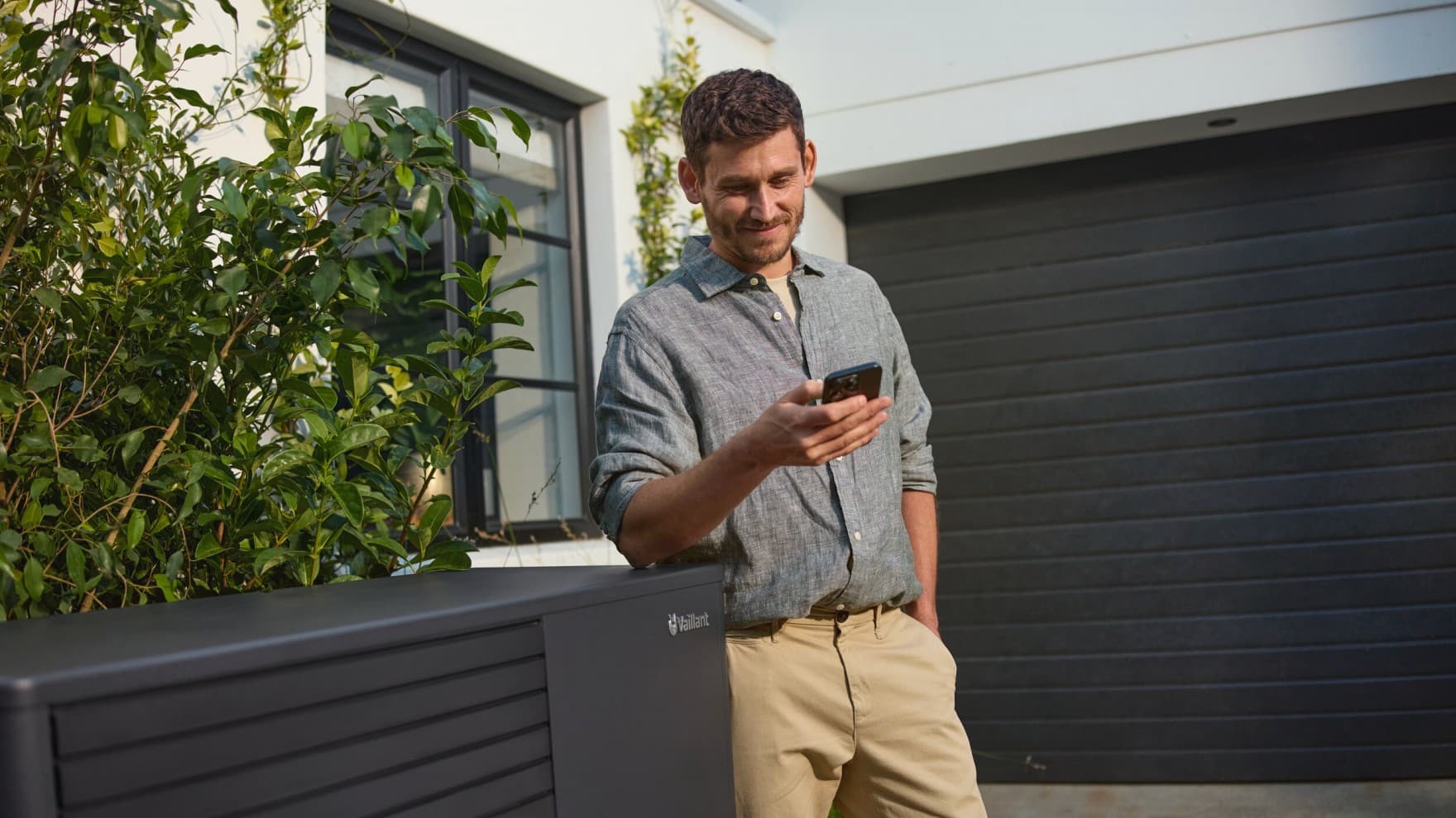 Mann neben Wärmepumpe mit Smartphone in der Hand